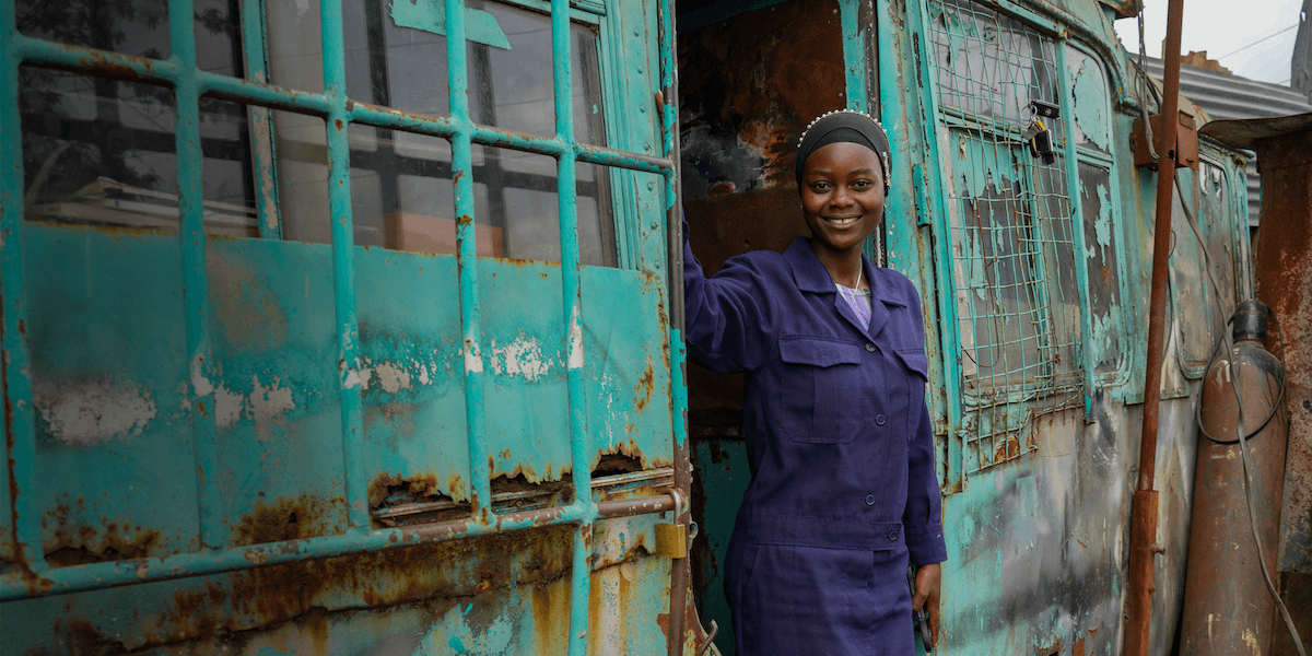 Ugwa standing in the door of a blue bus